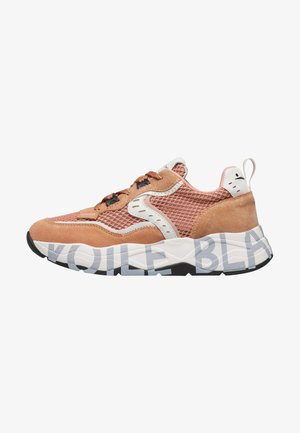 Chunky sneaker van perzikkleurig suède en mesh, met witte accenten, bruine veters en een dikke witte zool met grote grijze typografie.