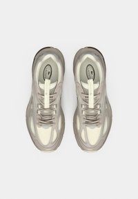 Chaussures de sport gris clair et beige avec un design texturé, tige en matériau synthétique et lacets. Présente un logo proéminent sur la languette.