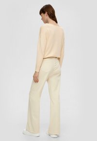 Pull en tricot beige clair avec une coupe décontractée, associé à un pantalon en denim flared de couleur claire et des baskets blanches. Texture subtile visible.