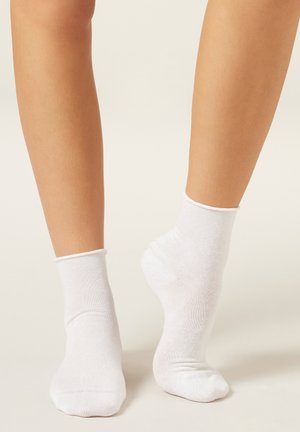 White cotton ankle socks, featuring a soft texture and ribbed cuff, positioned on bare feet with smooth skin visible.
