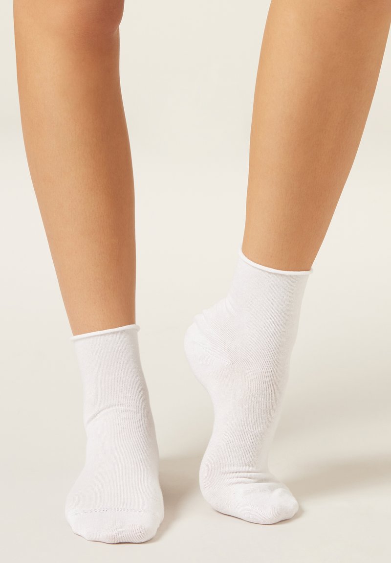 Chaussettes de cheville en coton blanc, avec une texture douce et un bord côtelé, portées sur des pieds nus avec une peau lisse visible.