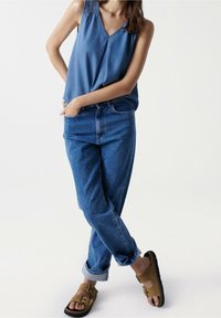 Světle modrý bezramínkový top s texturovanými detaily na ramenou, spárovaný s mid-modrými, volně střiženými džíny a hnědými sandály se sponou.