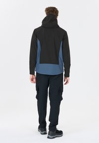 Schwarze und blaue wasserdichte Jacke mit Kapuze, die ein schlankes Design, eine glatte Textur und ein kontrastierendes unteres Panel aufweist. Kombiniert mit Cargo-Hosen.