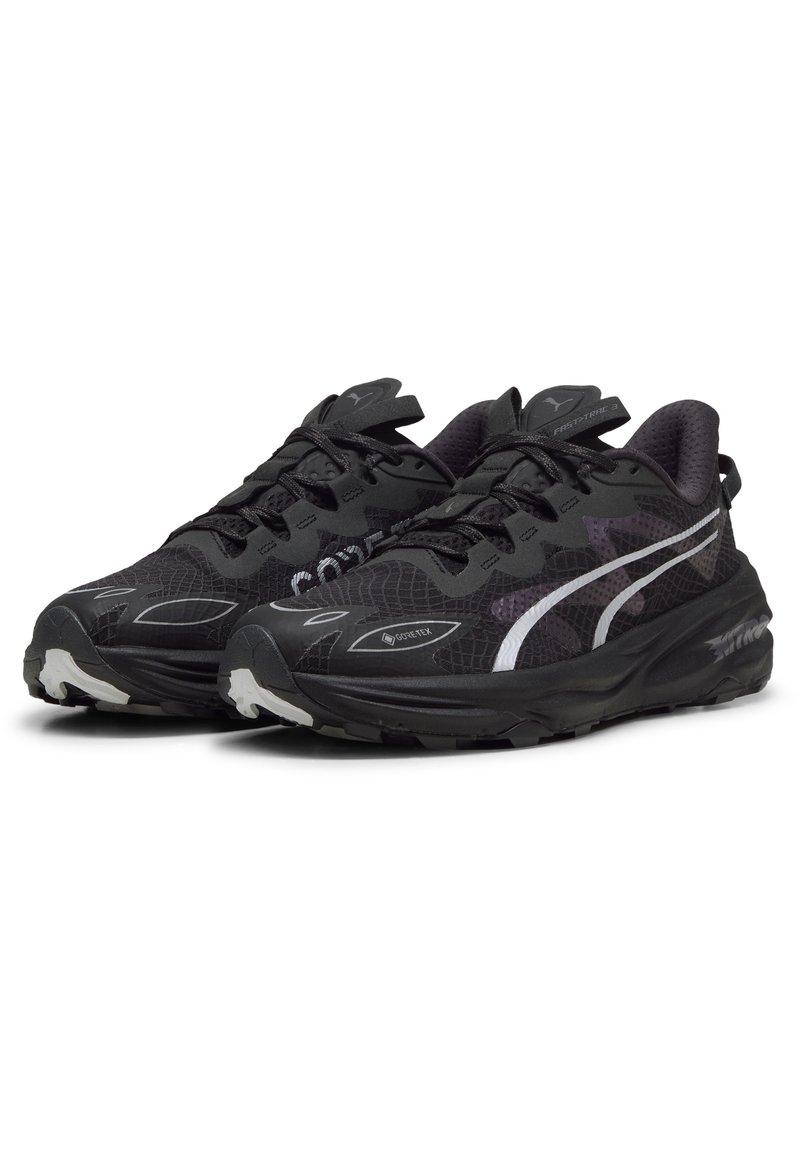 Des chaussures de sport noires avec une surface texturée, présentant une bande latérale blanche, des semelles rembourrées et un logo Gore-Tex pour l'imperméabilité.