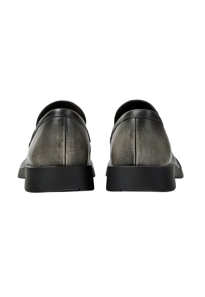 Paire de chaussures sans lacets gris métallisé avec semelles noires, vues de dos sur un fond blanc.