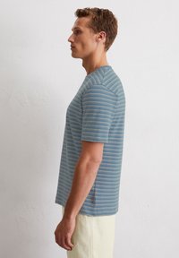 T-shirt à manches courtes rayé en bleu clair avec des lignes horizontales crèmes subtiles, doté d'un col rond et d'une texture douce.