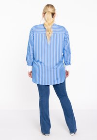 Blauw-wit gestreepte blouse met een ontspannen pasvorm, uitgerust met lange mouwen en een contrasterende witte kraag, gecombineerd met flared jeans.