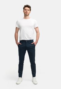 Navyblauwe slim-fit broek van lichtgewicht materiaal, met een knoopsluiting, zakken en witte sneakers gecombineerd met een plain wit t-shirt.