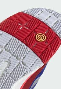 Running shoe outsole with a red textured section and a central yellow spiral detail. Features white and gray rubber patterns and red accents.