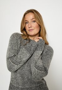 Sweter w paski z dzianiny w kolorze szarym z czarnymi akcentami. Posiada długie rękawy i ściągacze przy mankietach. Miękka faktura, luźny krój, wysoki kołnierz.