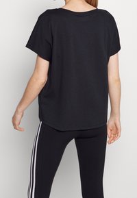 Svart bomull t-shirt med lös passform, korta ärmar och rundad halsringning, kombinerad med svarta leggings med vita sidostråk.