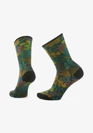 Calze alte fino al ginocchio con una base verde scuro caratterizzate da vivaci motivi di foglie in arancione, giallo e teal. Accenti neri sulla punta e sul tallone.