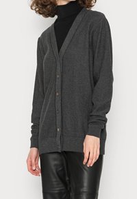 Grå cardigan gjord av mjukt material, med v-ringning, knappstängning, långa ärmar och ribbad nederkant och ärmslut. Bruna knappar pryder framsidan.