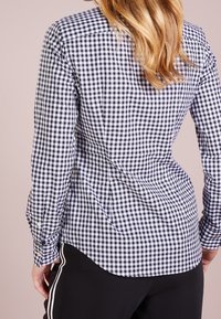 Svart- och vitrutigt skjort med lång ärm, knappmanschetter, böjd nederkant och slät tygtextur. Bärs med svarta träningsbyxor.