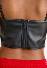 Top cropped em imitação de couro preto com fecho central em zíper e alças finas, apresentando uma textura suave e um design ajustado.