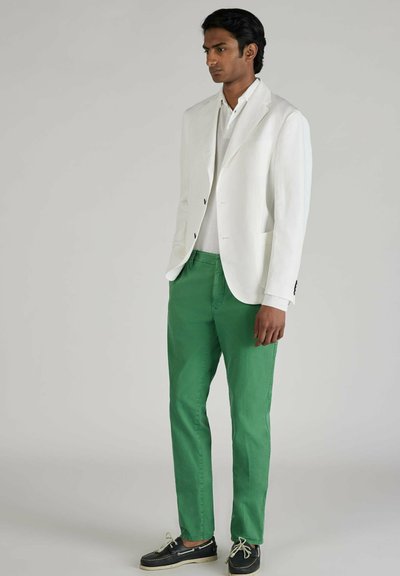 Blazer blanco de lino, pantalones de algodón verdes y zapatos oscuros. El blazer tiene dos botones, mientras que los pantalones son de corte recto y con un acabado suave.