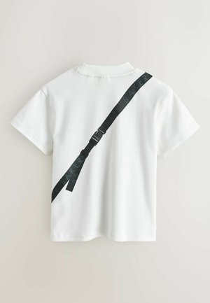 Valge lühikeste varrukatega särk, mille tagaosal diagonaalselt must rihm, millel kordub tekst "BAKER" ning metallist pandla.