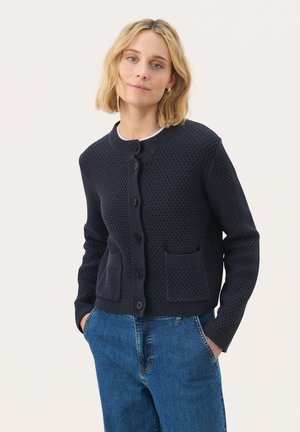 Merihenkinen neulottu cardigan, jossa on teksturoitu kuosi, pyöreä kaula-aukko, keskellä napit ja kaksi etutaskua. Yhdistettyinä sinisiin farkkuihin.