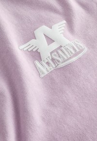 Hvidt "A" med vingelignende udvidelser og teksten "ALLSAINTS" broderet på lyse lilla stof.