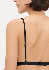 Black bralette with thin adjustable straps, a hook closure on the back, and a smooth, minimalist design. Skin tone background is neutral.