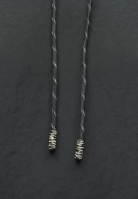 Czarne sznurki z teksturowanym wzorem, zakończone dwoma czarno-beżowymi prążkowanymi agletami.