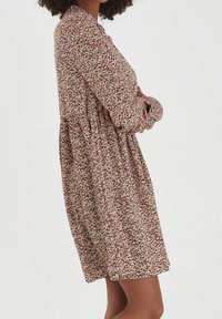 Abito a stampa floreale con maniche lunghe, collo a camicia e gonna svasata. I colori includono rosa, bianco e verde su uno sfondo scuro.