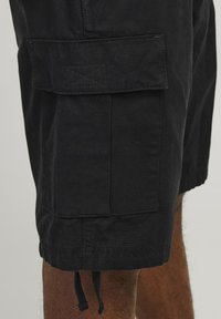 Sorte cargo shorts lavet af tekstureret stof, med sidelommer, forstærkede syninger og en justerbar snor i kanten.