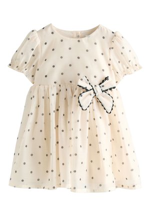 Crèmekleurige peuterjurk met grijze polkadots, pofmouwen en een zijstrik met zwarte biezen op de taille.