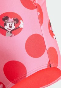 Roze badpakstof met grote rode stippen en cirkelvormige Minnie Mouse-graphics. Soepele textuur met rode accenten aan de zoom.
