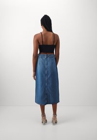 Džínová sukně s vysokým pasem a siluetou ve tvaru A, s ořezaným lemem a viditelným šitím, doplněná o přiléhavý černý crop top.