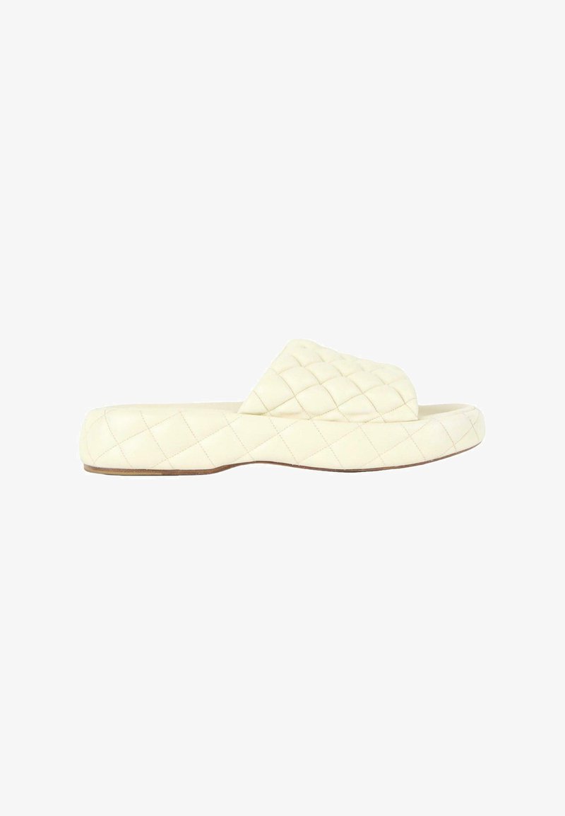 Sandale slide matelassée crème avec bride rembourrée et semelle plate, vue de côté sur fond blanc.