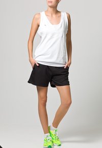 Top sin mangas blanco combinado con pantalones cortos deportivos negros. Zapatillas de deporte verde brillante con detalles en blanco. Diseño atlético simple y moderno.