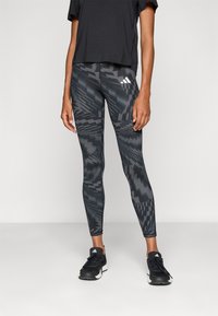 Sorte atletiske leggings med et geometrisk gråt mønster, tætsiddende design og høj talje. Sammen med en sort kortærmet top og sorte sneakers.