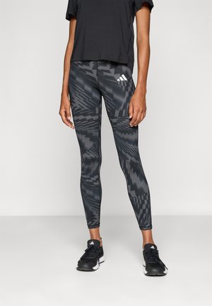 Black athletic leggings with a geometric gray pattern, fitted design, and high waist. Paired with a black short-sleeve top and black sneakers.