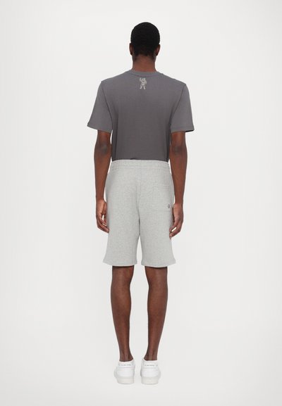 Grå t-shirt med korte ærmer og et lille grafisk motiv på ryggen, parret med lysegrå shorts. Behagelig, afslappet pasform med elastisk talje.