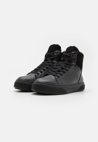 Sneakers negre înalte, cu partea superioară din piele și nubuc, vârf rotund, talpă texturată în contrast și șireturi negre. Fără logo-uri sau accente pronunțate.