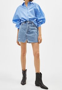 Blå randig skjorta med puffärmar, tillsammans med en sliten denimminikjol och svarta ankelstövlar.