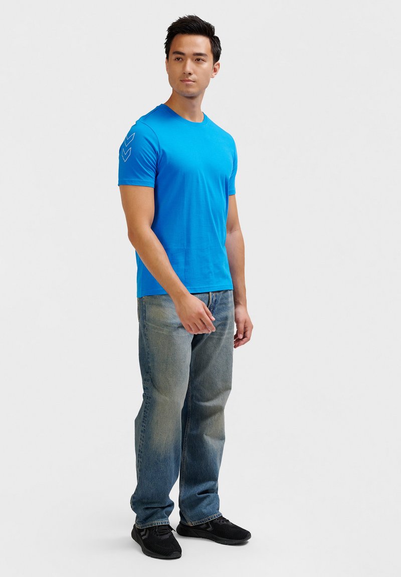 Blauwe T-shirt met korte mouwen van katoen, met een gladde textuur en zigzagpatroon op de linkerschouder, gecombineerd met lichte denim jeans.
