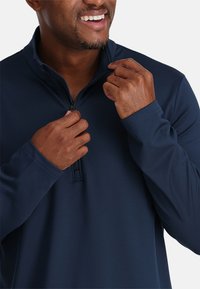 Marineblaues Zip-Pullover, leicht, mit hohem Kragen und langen Ärmeln. Der Stoff wirkt glatt mit minimalen Nähdetails.