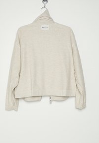 Pullover beige chiaro con colletto alto, maniche lunghe e dettaglio con zip sul retro. Tessuto morbido e vestibilità rilassata. Etichetta del marchio sul collo.