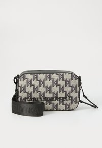 Kleine rechthoekige tas met een houndstooth-patroon in grijs en zwart. Beschikt over een logo aan de voorkant en een afneembare zwarte strap.