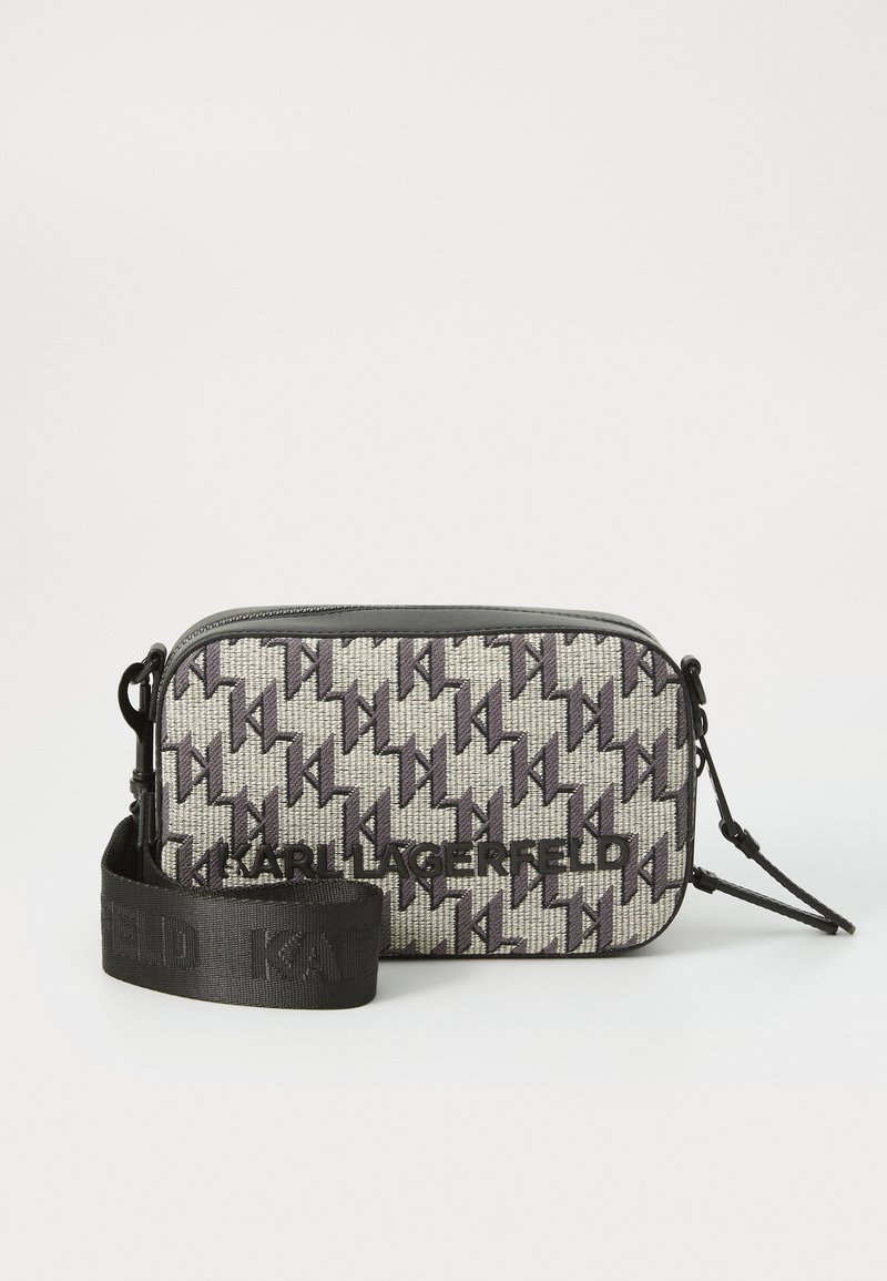 Kleine rechthoekige tas met een houndstooth-patroon in grijs en zwart. Beschikt over een logo aan de voorkant en een afneembare zwarte strap.