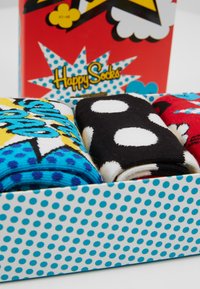 Three pairs of colorful socks in a polka dot gift box. Blue with yellow and black graphic design, black with white dots, and red with blue accents.