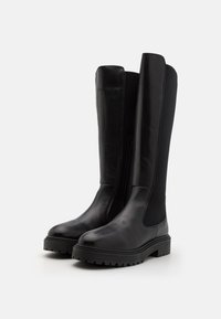 Botas negras de cuero y material elástico hasta la rodilla, con cremallera lateral, suela de goma gruesa y un acabado liso y mate.