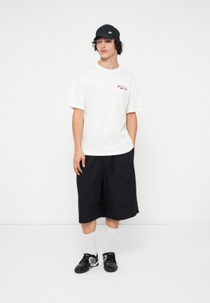 Hvid kortærmet t-shirt med et lilla logo, parret med sorte knælange shorts, sorte sneakers og hvide crew-sokker. Sort kasket.
