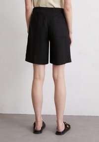 Schwarze Leinen-Shorts mit entspannter Passform, knielang, ausgestattet mit einer Gesäßtasche und einem elastischen Bund in mittlerer Höhe. Glatte Textur.