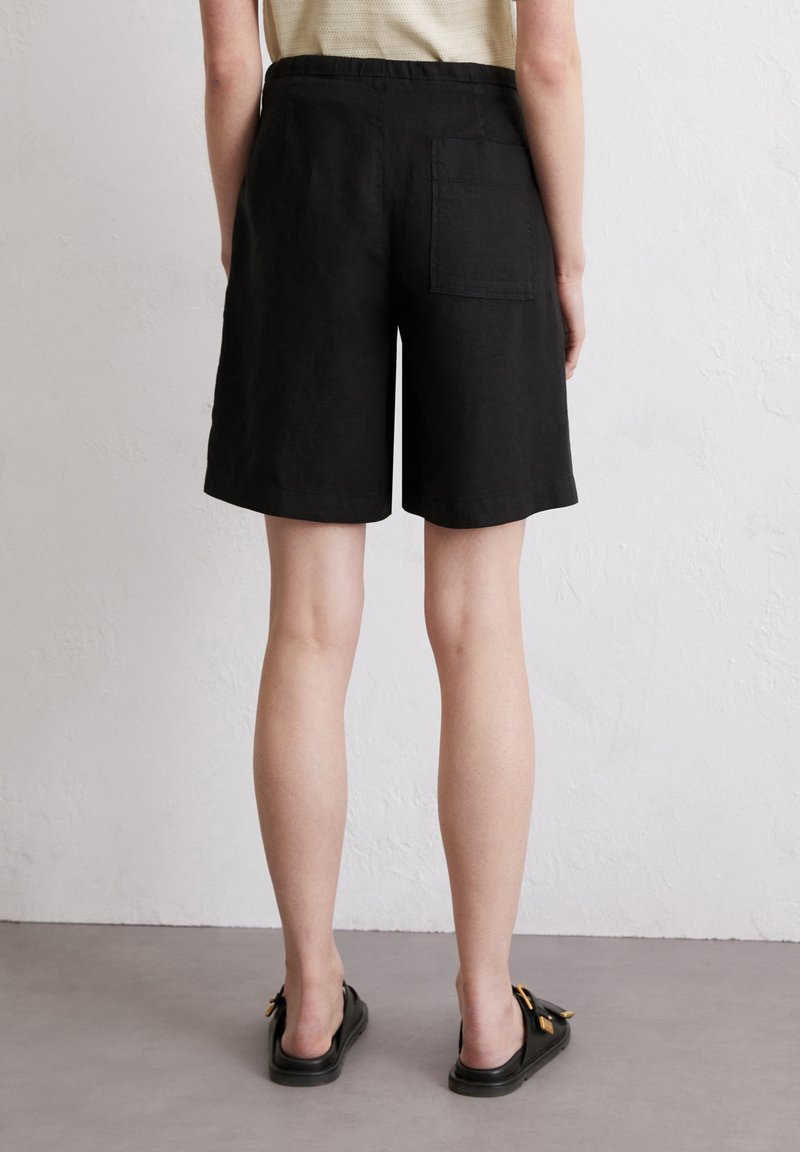 Schwarze Leinen-Shorts mit entspannter Passform, knielang, ausgestattet mit einer Gesäßtasche und einem elastischen Bund in mittlerer Höhe. Glatte Textur.