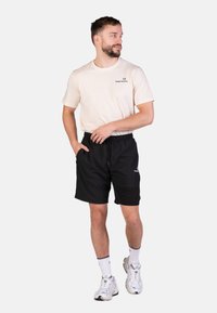 Schwarze Sportshorts mit einem elastischen Bund und Seitentaschen, kombiniert mit einem hellbeigen T-Shirt mit einem kleinen Logo auf der Brust.