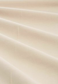 Tessuto di cotone beige con una superficie liscia, caratterizzato da morbide pieghe e grinze. Il materiale è leggero e uniforme nel colore.