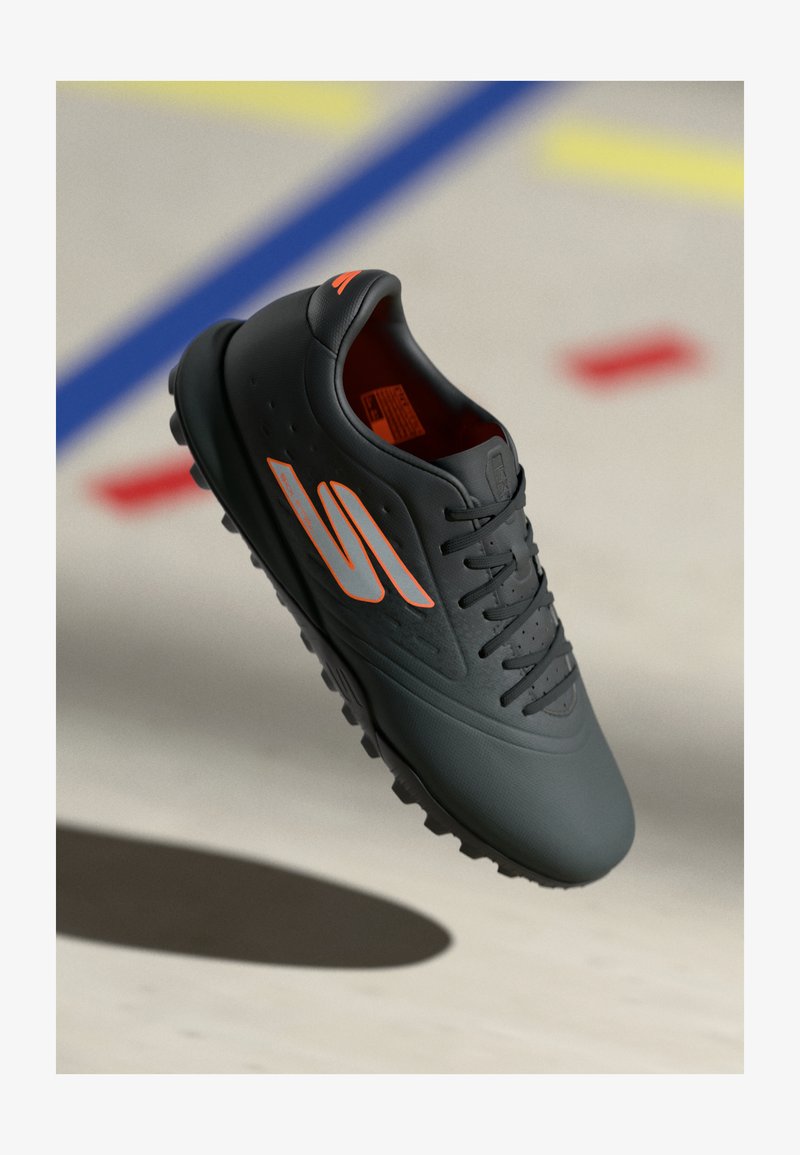 Baskets de sport noires avec une finition lisse et mate, présentant des accents orange et une semelle texturée pour l'adhérence. Lacets et détails de ventilation inclus.